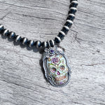 La Catrina Sugar Skull  Pendant Set In Sterling Silver with Purple Faceted Stone hung on navajo pearl nacklace copyright chisholm trail designs 2025